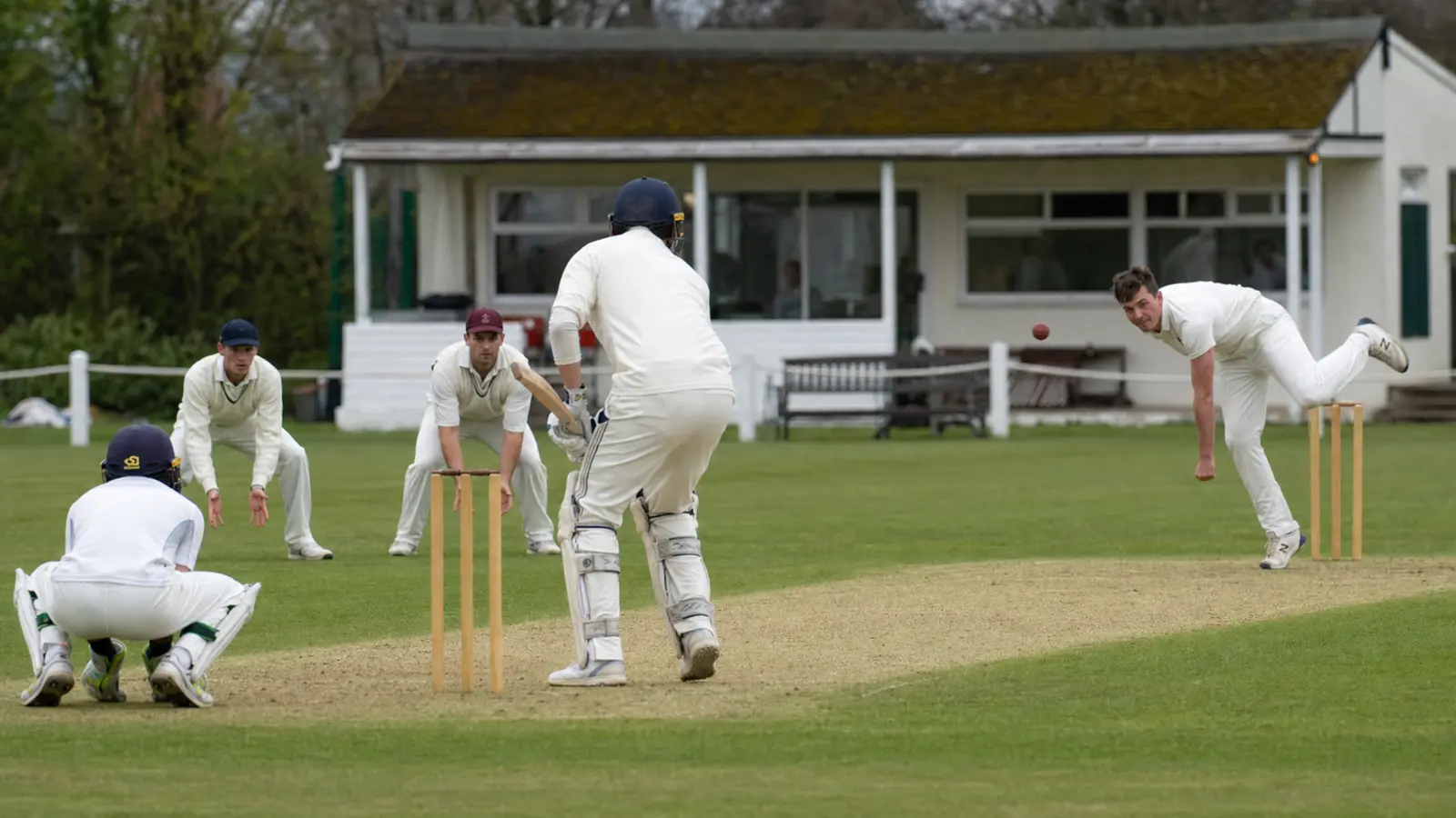 Medium view of a club cricket match in play with the bowler, batsman and slip fielder visible around the wicket